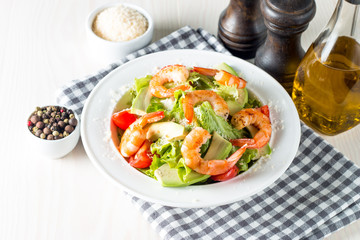Fresh shrimp salad made of tomato, ruccola, avocado, prawns, chicken breast, arugula, crackers and spices. Caesar salad in a white, transparent bowl on wooden background