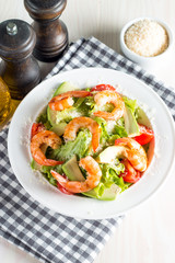 Fresh shrimp salad made of tomato, ruccola, avocado, prawns, chicken breast, arugula, crackers and spices. Caesar salad in a white, transparent bowl on wooden background