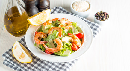 Fresh shrimp salad made of tomato, ruccola, avocado, prawns, chicken breast, arugula, crackers and spices. Caesar salad in a white, transparent bowl on wooden background