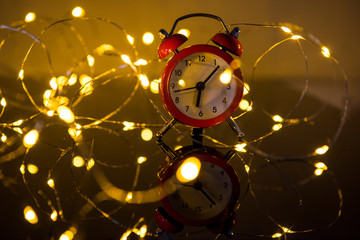 Alarm Clock And Christmas Lights Against Blurred Background. Winter Night