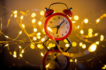 Alarm Clock And Christmas Lights Against Blurred Background. Winter Night