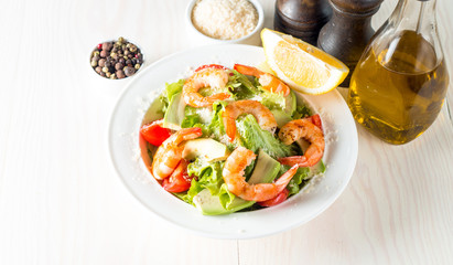 Fresh shrimp salad made of tomato, ruccola, avocado, prawns, chicken breast, arugula, crackers and spices. Caesar salad in a white, transparent bowl on wooden background