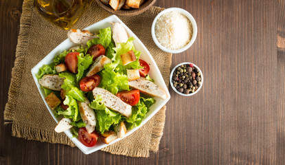 Fresh salad made of tomato, ruccola, chicken breast, eggs, arugula, crackers and spices. Caesar salad in a white, transparent bowl on wooden background