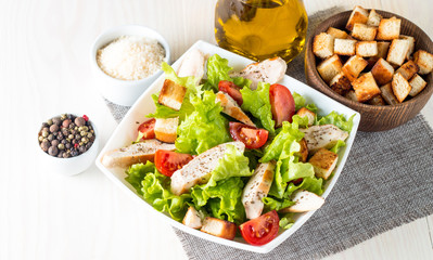 Fresh salad made of tomato, ruccola, chicken breast, eggs, arugula, crackers and spices. Caesar salad in a white, transparent bowl on wooden background