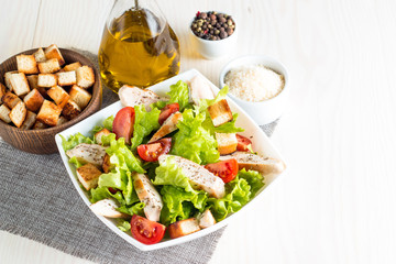 Fresh salad made of tomato, ruccola, chicken breast, eggs, arugula, crackers and spices. Caesar salad in a white, transparent bowl on wooden background