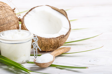 Coconut oil in airtight glass jar spoon and shell pieces on white wooden table