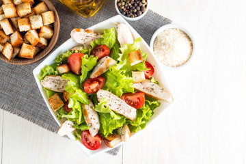 Fresh salad made of tomato, ruccola, chicken breast, eggs, arugula, crackers and spices. Caesar salad in a white, transparent bowl on wooden background