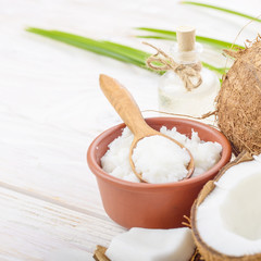 Background of coconut, coconut shell, oil in clay bowl and glass jar and spoon on white wooden table