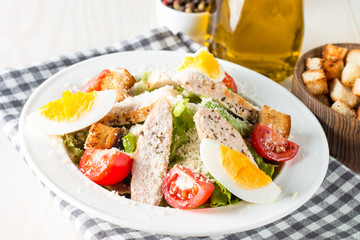 Fresh salad made of tomato, ruccola, chicken breast, eggs, arugula, crackers and spices. Caesar salad in a white, transparent bowl on wooden background
