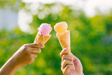 woman holding and eating ice cream in the park. Hands holding melting ice cream waffle cone in hand on summer nature light  background. Two colorful tasty ice cream cones in hand.