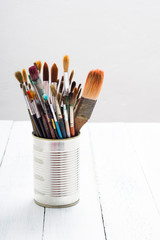 bunch of paint brush at tin can, on white wooden