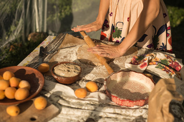 woman in gentle sundress cooking a sweet pie with fresh apricots on a sunny summer day