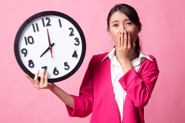 Sleepy young Asian woman with a clock in the morning.