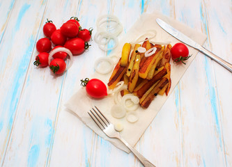 Fototapeta na wymiar Home made potato food with tomatos cherry and onion . Baked potatoes with spices and salt on white wooden background. Fork and knife on the kraft paper. Top view