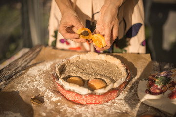 woman in gentle sundress cooking a sweet pie with fresh apricots on a sunny summer day