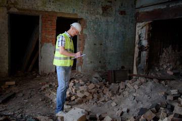 A man in a construction helmet and with a black folder in his hands at a construction site. The brigadier in a working form, examination of the structure.