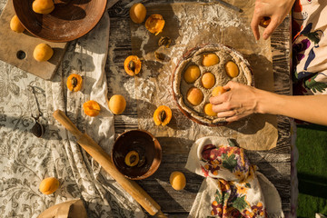 woman in gentle sundress cooking a sweet pie with fresh apricots on a sunny summer day