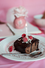 tasty homemade chocolate birthday cake decorated of some raspberries and candles served on the gentle pink background
