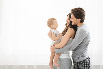 Young millennial couple standing with baby at window at home