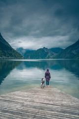 Kobieta z psem Springer Spanielem stoją na drewnianym pomoście nad górskim jeziorem Traunsee w Austrii w pochmurny dzień	