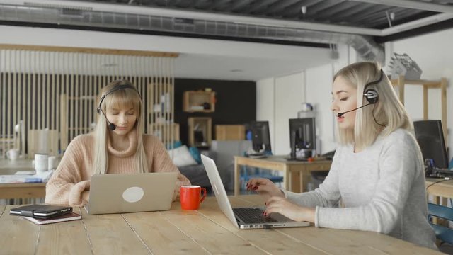 Attractive businesswomen wear headsets talking looking at laptop, female customer support manager skyping