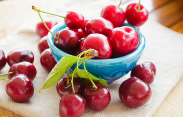 Bright juicy red berries and leaves of sweet cherry in a blue enamelled ceramic bowl. Close-up, selective focus image.