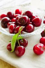 Bright juicy red berries and leaves of sweet cherry in a small glass bowl. Close-up, selective focus image.