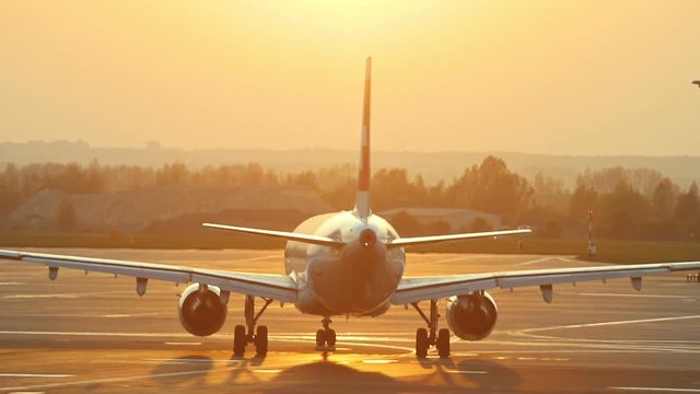 A huge plane is moving on the airport runway on a background of orange sunset