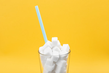 Glass of sugar cubes on a yellow background. Sweet food ingredient for cooking, baking, and beverages. Intake of bad calories.
