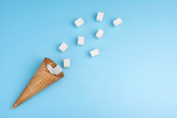 Flying sugar. Waffle cone with refined sugar on blue background. Cone full of refined sugar. Diet concept. Cone for ice cream full of sugar as symbol of high calorie unhealthy nutritio.