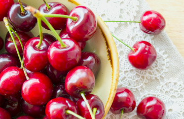 Bright juicy red berries and leaves of sweet cherry in an enamelled ceramic bowl. Close-up, selective focus image.