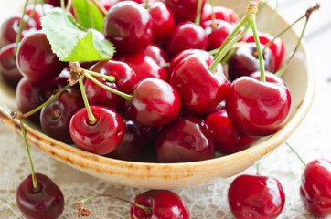 Bright juicy red berries and leaves of sweet cherry in an enamelled ceramic bowl. Close-up, selective focus image.