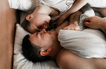 Obraz na płótnie Canvas Young couple in hotel. Family waking up in the morning on bed. Cute couple waking up after a night sleep. Happy couple flirting and speaking in the morning on a comfortable bed at home. Relaxing after