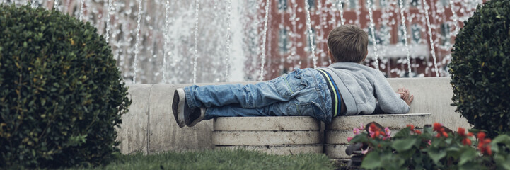 Toddler boy lying in front of a water fountain