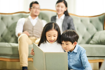 two asian children reading book together