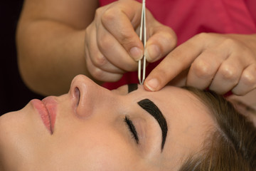 Young woman having professional eyebrow correction procedure in beauty salon