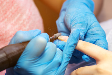 Closeup hardware manicure in a beauty salon. Manicurist use electric nail file drill to manicure on fingers.