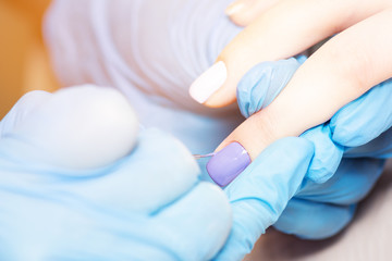 Closeup healthy natural woman's nails in beauty salon. Manicurist hand painting client nails. Covering nails with gel