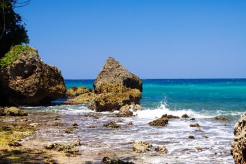 Fototapeta na wymiar View beyond sharp rocks on turquoise rough sea with wave breakers and strong surf - Port Antonio, San San beach, Jamaica