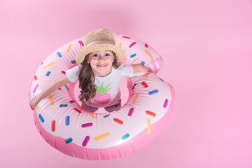 A little child girl lying on a donut inflatable circle. Pink background. Top view. Summer concept.
