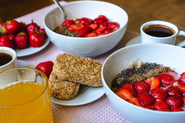 Closeup of vegan superfood breakfast: bowls of oatmeal porridge with strawberries and Omega 3 seeds, cereal biscuits, coffee and fresh orange juice. Healthy plant based diet, health and diet concept.