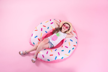 A little child girl lying on a donut inflatable circle. Pink background. Top view. Summer concept.
