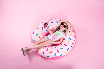 A little child girl lying on a donut inflatable circle. Pink background. Top view. Summer concept.