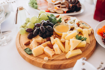 cheese plate with a bunch of grapes, honey and nuts. Gouda, parmesan, mozzarella, gorgonzola on a wooden board.