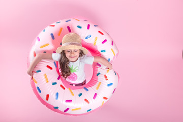 A little child girl lying on a donut inflatable circle. Pink background. Top view. Summer concept.