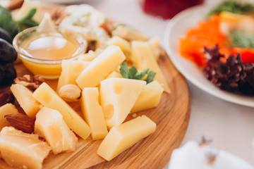cheese plate with a bunch of grapes, honey and nuts. Gouda, parmesan, mozzarella, gorgonzola on a wooden board.