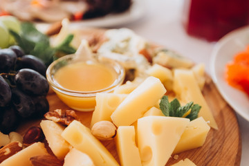 cheese plate with a bunch of grapes, honey and nuts. Gouda, parmesan, mozzarella, gorgonzola on a wooden board.