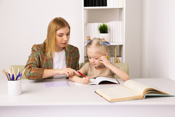 Mother doing homework with daughter indoor sitting on the desk