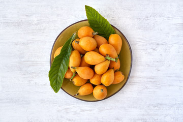 Loquat fruit. Nispero. Eriobotrya Japonica. Loquat in plate with fresh leaves on wood background	