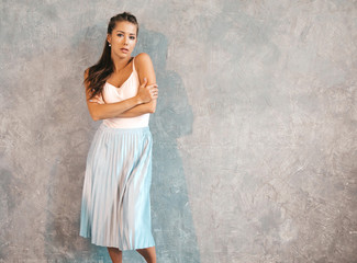 Young beautiful woman looking at camera. Trendy girl in casual summer dress . Funny and positive female posing near gray wall in studio and giving kiss